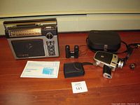 Overview of all items together on wood floor including binoculars, radio, camera, manual, and cases