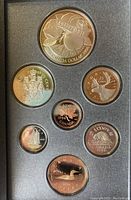 Photo of obverse sides showing animal and commemorative designs including McIntosh apple on silver dollar and other coins arranged in foam casing