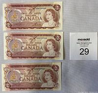 Full view of three sequential Canadian $2 bank notes from 1974 laid flat showing front designs and serial numbers.
