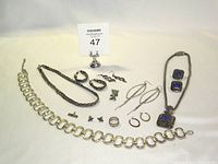 Full view of the lot showing all jewelry pieces on a light background, including chunky silver bracelet, braided chain necklace and bracelet, several pairs of earrings, and pendant necklace with purple stones.