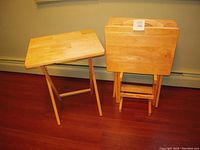 Four solid wood rectangular TV trays with patchwork wood block tops. One tray set up, three nested and standing vertically with foldable legs and handle cutouts visible. Natural light wood finish.