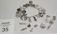 Overall image of the sterling silver charm bracelet with most charms attached and some loose on a light-colored surface.