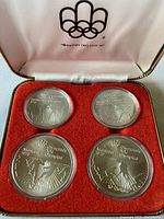 Four coins in red velvet interior of presentation case under white satin lid with Olympic rings logo
