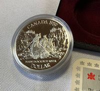 Close-up of the silver dollar coin showing intricate design of Sir Alexander Mackenzie and companions in a canoe, with Canadian river and forest scenery.