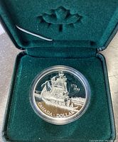 Close-up of the sterling silver proof dollar coin showing detailed design of the ship 'The Santiago' with inscriptions 'Canada Dollar' and dates '1774-1999'. Coin is in protective plastic capsule inside green velvet case with maple leaf embossing.