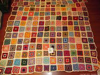 Full view of the vintage crochet afghan blanket showing the entire patchwork of colorful granny squares bordered in white.