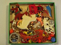 Top view showing mixed assortment of vintage brooches and pins with various shapes including animal figures, floral designs, and novelty items in a green box.