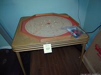Wooden octagonal Crokinole game board on metal folding legs with bag of poker chips on board.