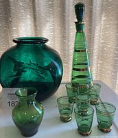 Wide shot showing all items: large round vase, smaller vase, liqueur decanter, and six shot glasses with gold bands.