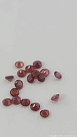 Close-up of multiple small natural red garnet gemstones spread on a plain surface, showing facets and color.