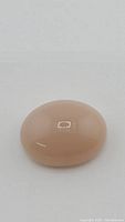 Close-up photo of the smooth, oval-shaped peach moonstone with visible highlight and reflection on surface.