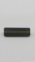 Rectangular baguette cut green tourmaline gemstone on plain background showing dark green color and facet edges.