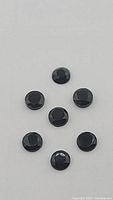 Top view of seven round jet black onyx gemstones arranged on a plain surface showing faceted rose cut details and uniform sizing.