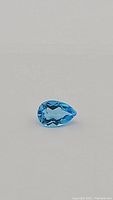 Close up photo showing deep blue pear cut Swiss blue topaz gemstone with facets clearly visible.