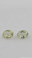 Front view of two oval cut mint green sillimanite gemstones placed side by side on gray background.