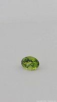 Close-up photo of the oval cut apple green peridot gemstone on a grey background, showing the clean facets and color.