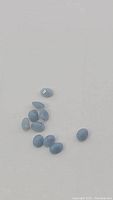 Top view of 10 small oval blue opal cabochon gemstones on white background.