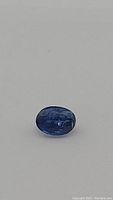 Close-up photo of a single oval cut kyanite gemstone on a white background, showing its blue color and inclusions.