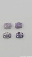 Close-up of four lilac purple opal cushion cabochon gemstones showing color variations and crackled patterns.