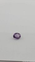 Oval cut natural purple amethyst gemstone on a plain white background, showing top facet and depth of color and clarity.