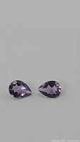Close up photo showing two purple pear-cut amethyst gemstones side by side.