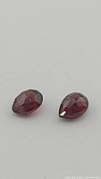 Close-up photo of two pear-shaped cherry red garnet gemstones showing checkerboard cuts and deep red color