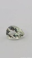 Close-up photo of natural prasiolite green amethyst pear cut gemstone on white background showing facets and clarity.