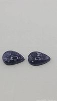 Two pear-shaped purple opal cabochon stones with polished glossy surface on a white background.