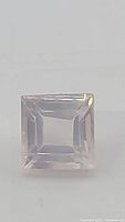 Close-up photo of a square cut rose quartz gemstone viewed from the top showing faceting and clarity.