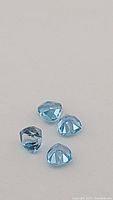 Close-up photo of four vibrant lagoon blue Swiss blue topaz gemstones, trillion cut facing up showing facets.