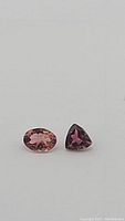 Close-up photo of two loose cut tourmaline gemstones, one oval cut pinkish-brown and one trillion cut purple.