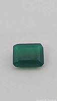 Close-up photo of the vivid green onyx emerald cut gemstone, showing color and cut details.