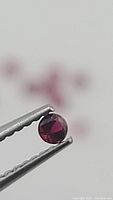 Single round ruby held by tweezers against white background