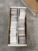 Top-down view into a divided cardboard box containing a large quantity of baseball trading cards, mostly organized vertically in two rows.