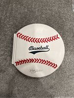 Front cover of the book shaped like a baseball with red stitching detail and the word 'Baseball' on it.