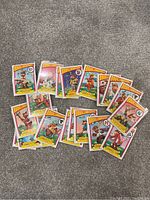 Photo showing 13 colorful Bouillabaseball trading cards with various cartoon baseball player illustrations arranged on a carpeted floor.