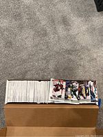 Top-down photo showing a large stack of hockey trading cards on a carpeted floor: one smaller stack of visible front-facing cards with player images, and one larger stack of cards mostly facing down showing card backs
