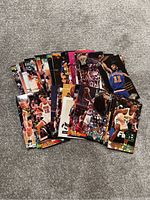 Photo showing 22 basketball trading cards laid out on a carpeted floor. Cards depict different NBA players in game action.