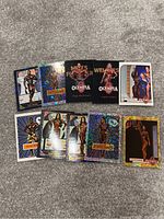 Photo of 10 Olympia trading cards laid out on carpet, showing various male and female bodybuilders, holographic and foil finishes, some with numbered 1/1 and 10/10 editions.