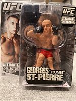 Photo of Georges St-Pierre UFC Ultimate Collector Series 1 action figure in original closed packaging with visible soiling and wear.