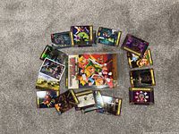 Top-down view showing 18 colorful Zelda themed trading cards arranged in a circle around a collector's book on carpeted floor.