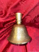 Front view of the antique engraved brass pipe base with intricate floral and geometric patterns on red fabric background.