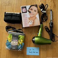Hair styling tools and beauty items including curling iron, hair dryer, hot rollers, laser hair remover box, and cosmetic pouch on wooden floor.