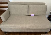 Front view of beige Crate & Barrel loveseat showing seat and back cushions and textured fabric upholstery.