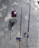Two fishing rods with reels and a fishing net displayed on pavement.