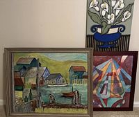 Framed oil painting of a coastal village scene with cottages, dock, two people, and boats in cubist technique, alongside two other artworks partly visible.