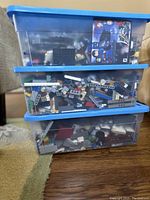 Three stacked clear plastic storage bins with blue lids filled with assorted LEGO bricks and partial build instructions visible inside.