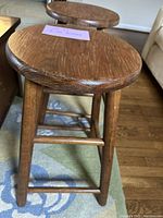 Close-up of one oak barstool's round seat and legs, highlighting wood grain and condition