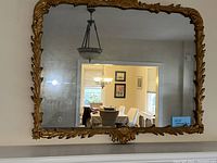 Full view of large rectangular vintage mirror framed in elaborate gold carved wood, hanging on a wall reflecting dining room.
