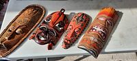 Photo shows four carved wooden masks laid flat on a white surface. Each mask features unique colors and patterns.